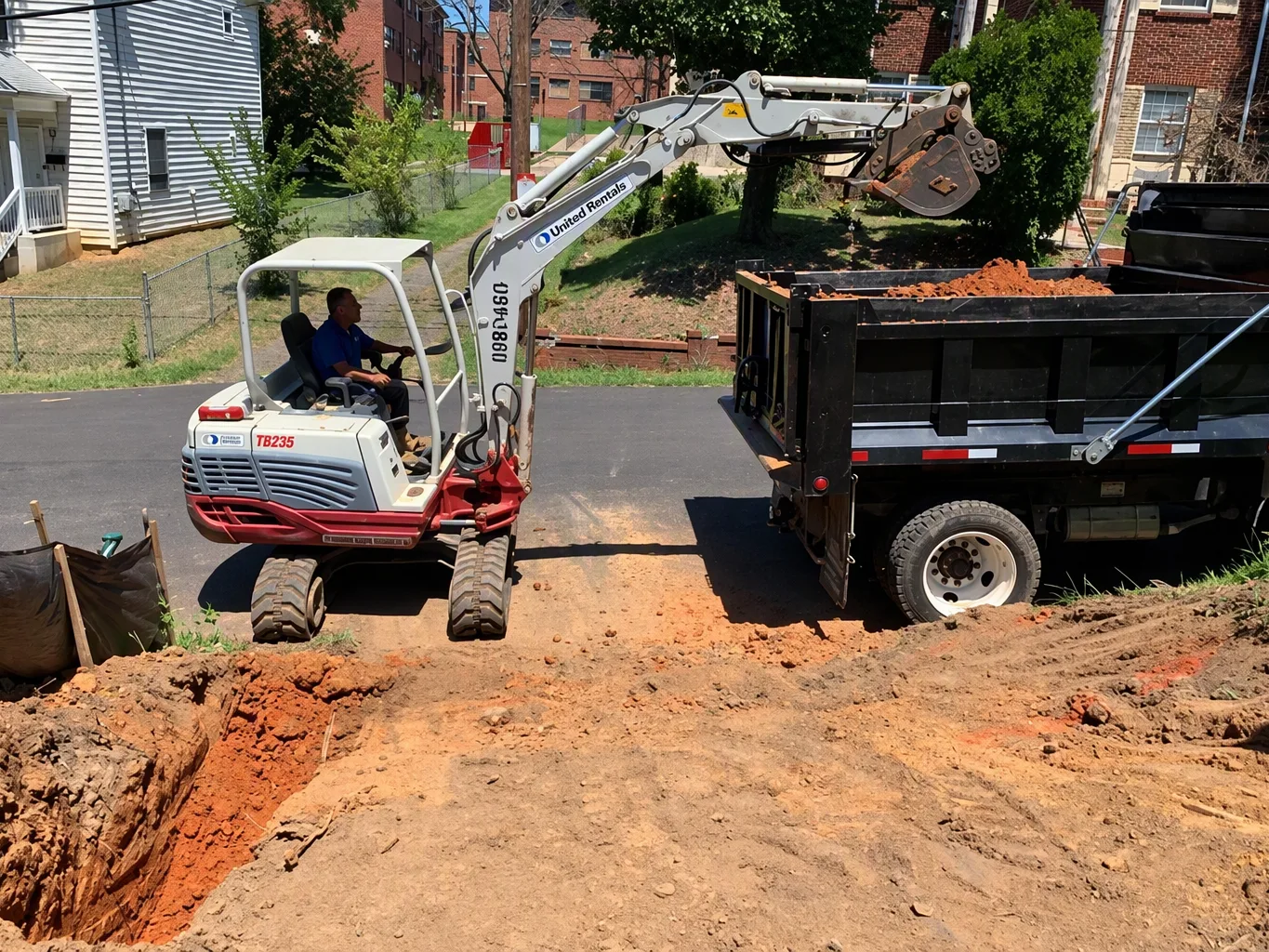 During site grading, a worker operates a compact track loader to spread fill across a cleared building area, watching the bucket and grade rather than the camera
